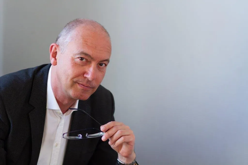 Reinhard Giese im dunklen Sakko, die Brille in der Hand, lächelt in die Kamera